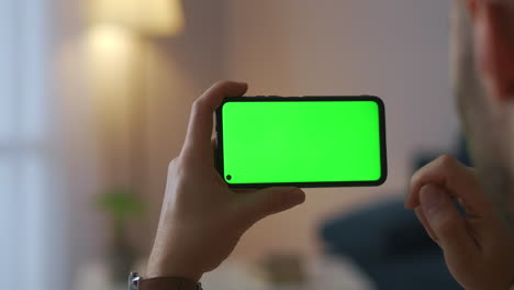 male-user-is-using-new-application-in-smartphone-holding-gadget-horizontally-green-screen-technology-for-montage-closeup-view-indoors